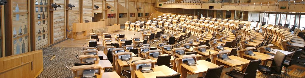 A view towards the podium from the behind the last chair on the back row of the left of the debating chamber in the Scottish parliament