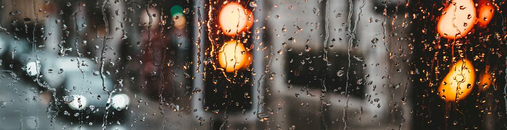 Raindrops on window looking out over a urban road junction, with blurred traffic in the background