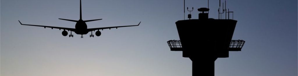The silhouettes of a plane next to an airport tower at dawn. The silhouettes of a plane next to an airport tower at dawn.