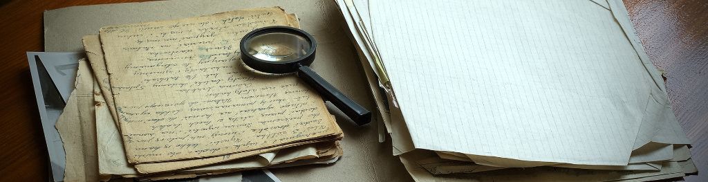 Old, yellowed papers marked with cursive handwriting, with a magnifying glass resting on the top. Old, yellowed papers marked with cursive handwriting, with a magnifying glass resting on the top.