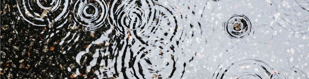 A puddle on a gravelled surface with raindrops hitting it, creating a pattern of concentric circular ripples on its surface. A puddle on a gravelled surface with raindrops hitting it, creating a pattern of concentric circular ripples on its surface.