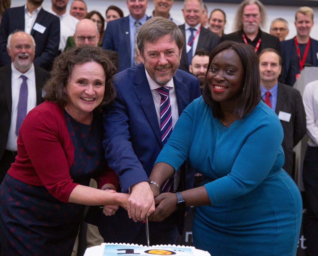 Met Office Chief Executive Penny Endersby, Met Office Head of Space Weather Mark Gibbs and Parliamentary Secretary at the Cabinet Office Abena Oppong-Asare MP cutting a cake with '10' iced on to mark the 10th anniversary of MOSWOC.