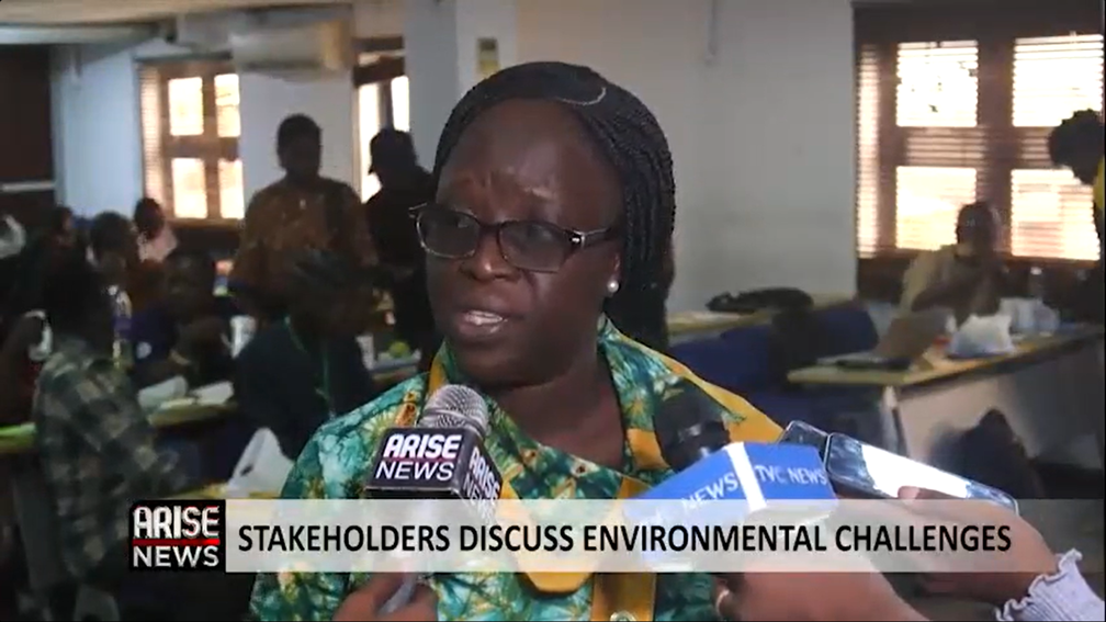 A woman speaking into news microphones with TV news graphics overlaid reading 'Stakeholders discuss environmental challenges'.