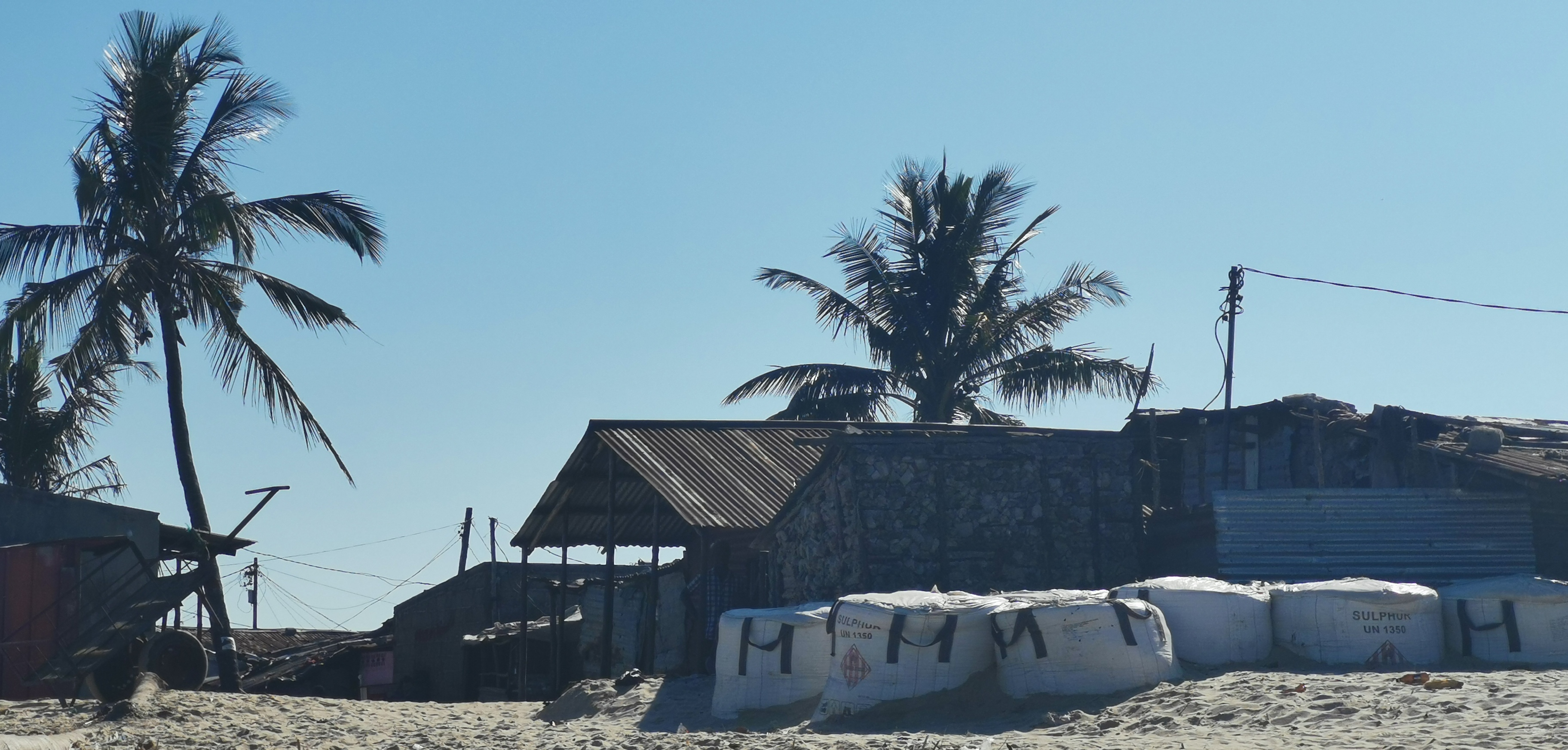 Basic buildings in a southern African town with palm tress and a sandy ground.